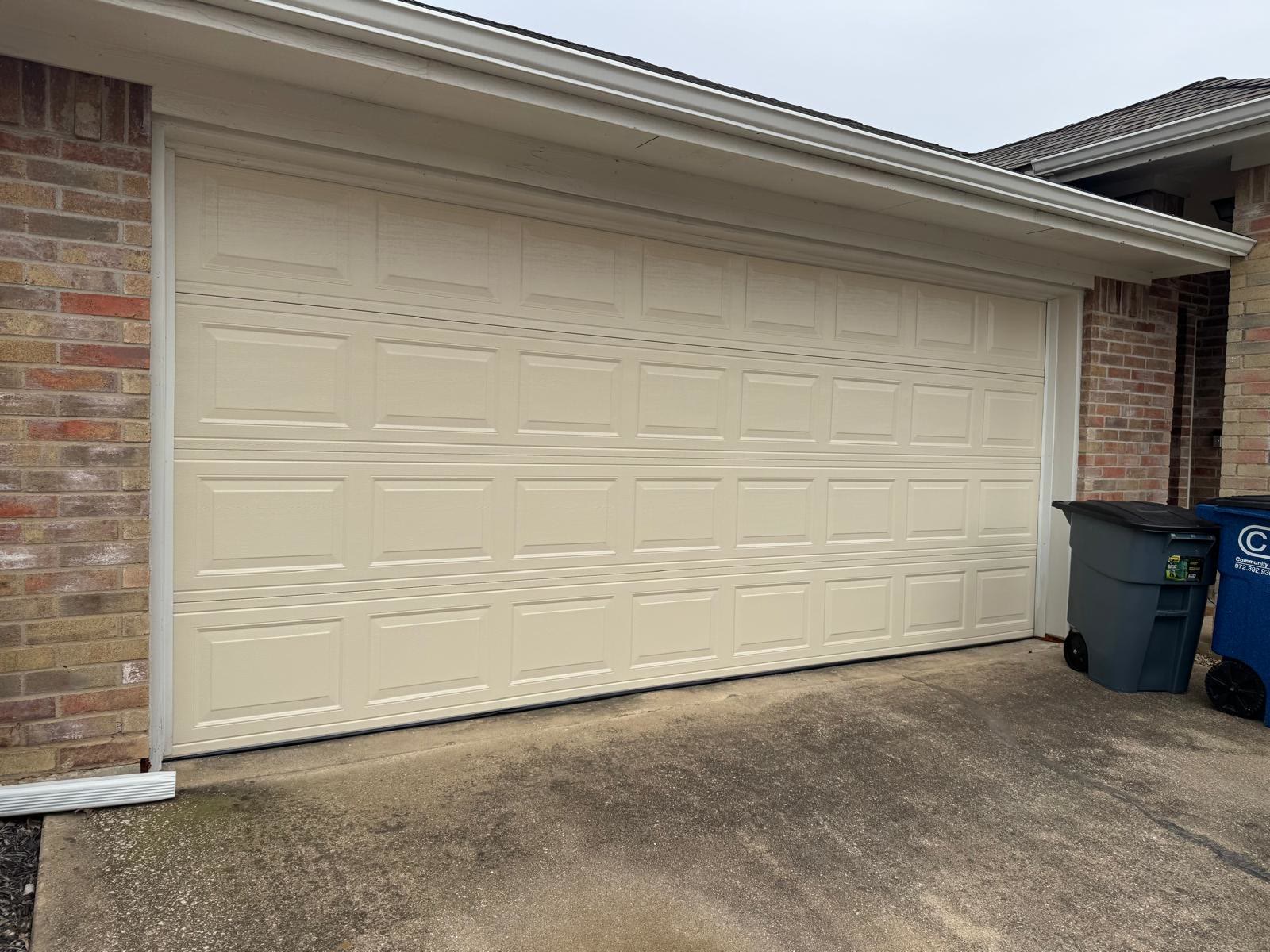 Almond short-panel double garage door closed on a brick home on an overcast day, photographed square-on from the driveway.