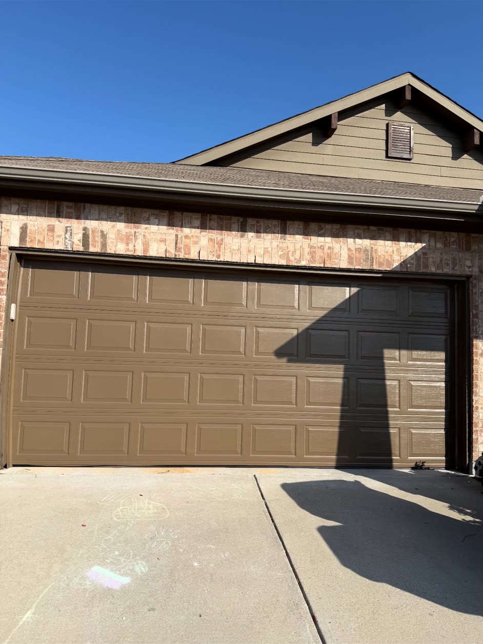 Tan short-panel double garage door on a brick home under a clear blue sky, with children's chalk drawings on the driveway in front.